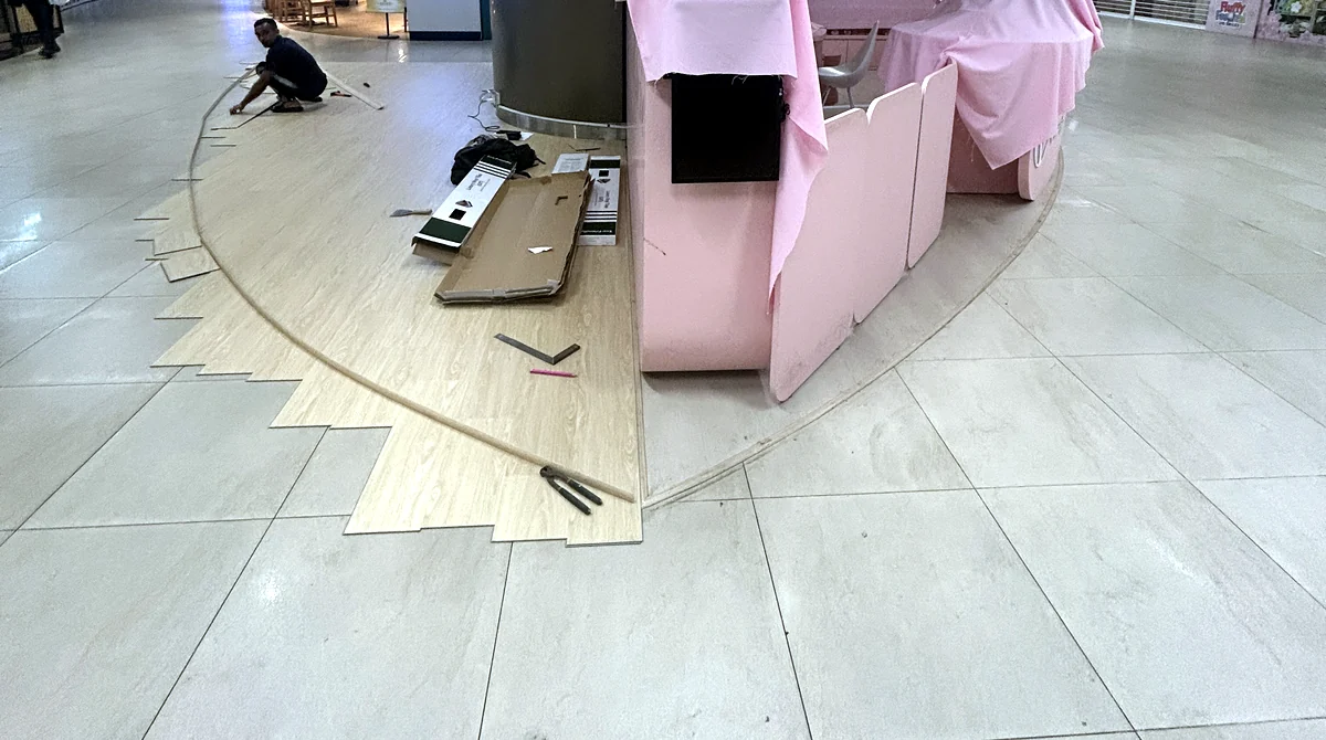 Commercial flooring in Singapore: wood-look vinyl planks being laid around a retail kiosk in a shopping mall