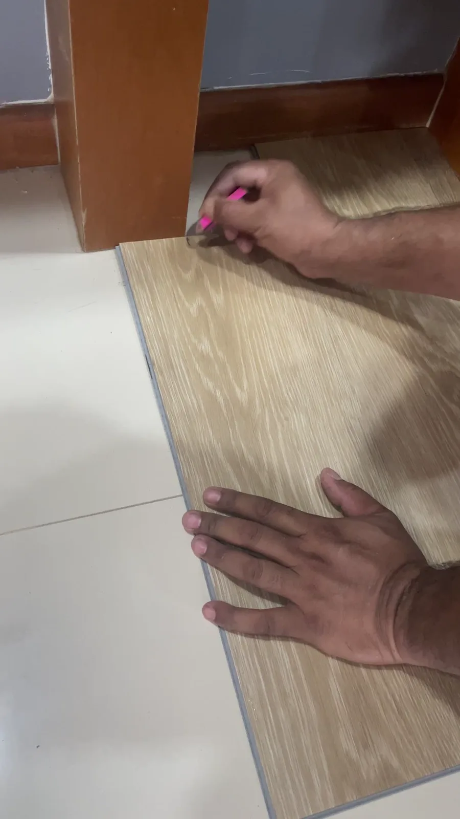 Vinyl plank being laid directly over existing white floor tiles in a Sengkang HDB flat