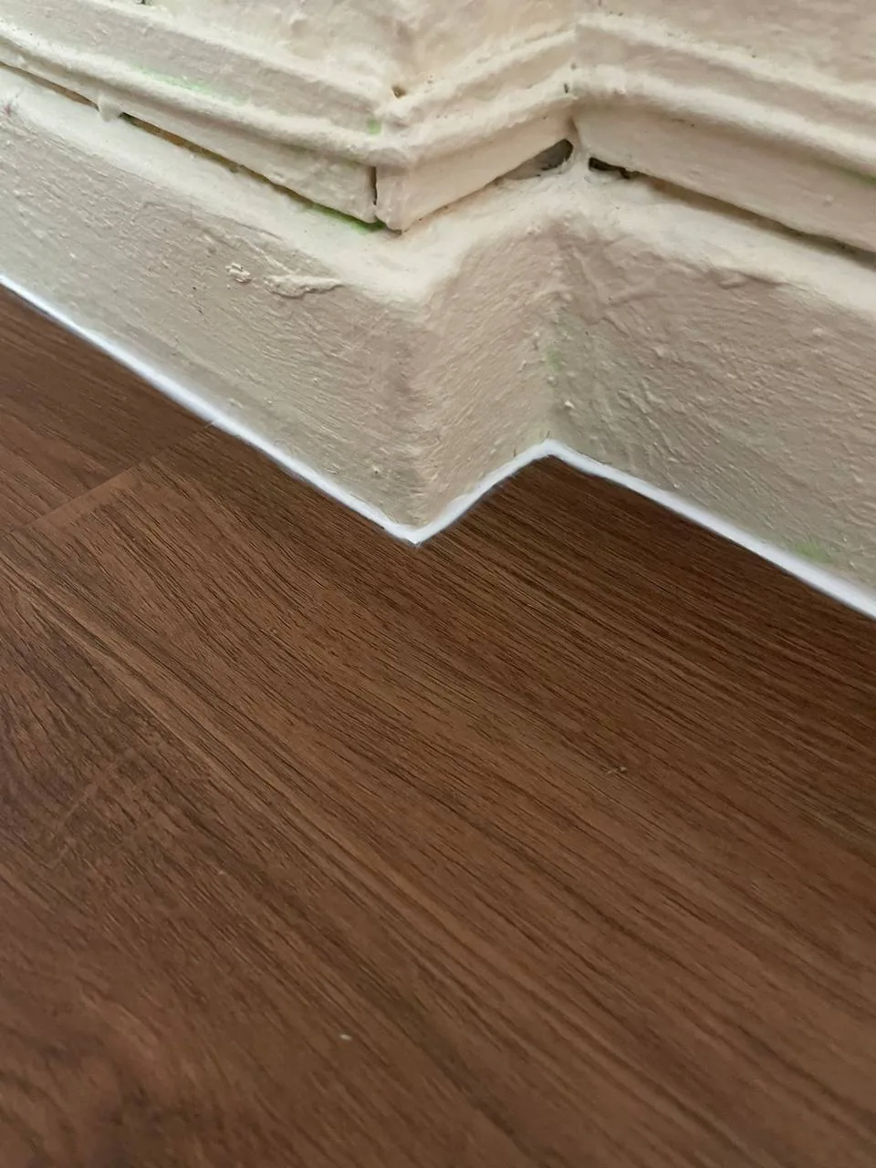 Close-up of dark walnut LVT vinyl meeting a painted skirting at an internal corner