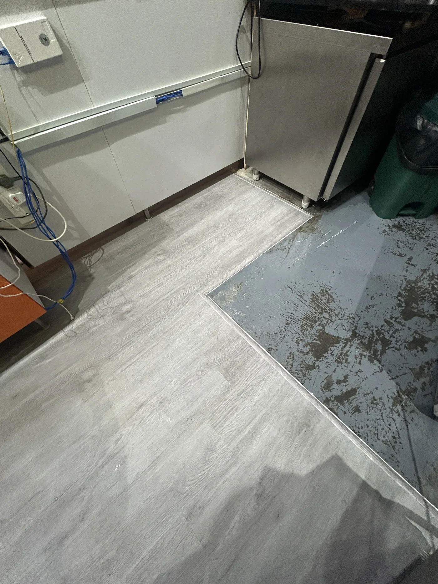 Grey wood-look vinyl flooring part-laid in a commercial back-of-house kitchen area