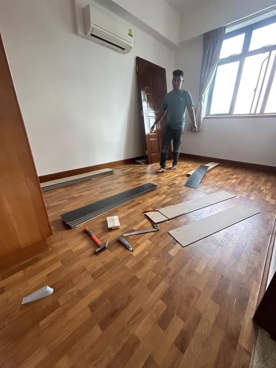 LN installer standing on an existing parquet floor with pale vinyl planks and hand tools laid out ready to overlay