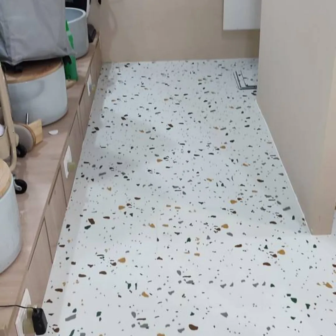 White terrazzo-look floor speckled with grey, green and ochre chips, running beside a row of low timber cabinets