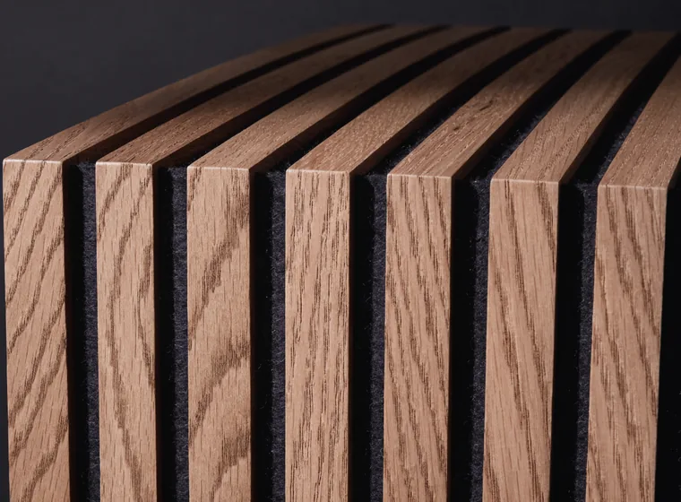 Macro close-up of a slat wall panel: square oak battens with open gaps showing dark felt backing